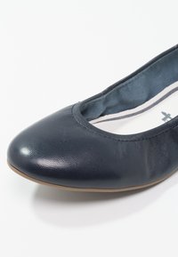 Marinblå läderballettskor med rund tå, slät yta och sydd kant. Mjuk inredning med subtilt mönster.