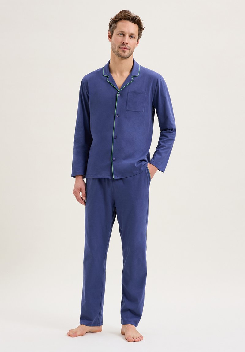 Ensemble de pyjama bleu marine en tissu doux, comprenant un haut à bouton avec une poche et une passepoil vert contrastant, assorti à un pantalon.