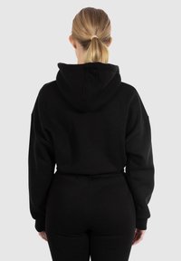 Sudadera con capucha negra hecha de una tela suave, que presenta un corte relajado y puños acanalados. Sin logotipos ni patrones visibles.