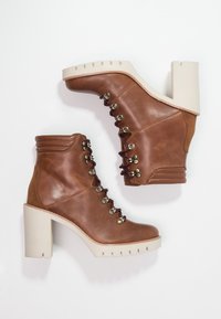 Bottines en cuir marron avec un haut talon carré, design à lacets, œillets métalliques et semelle texturée. Comprend un bout rond et des accents cousus.