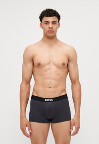 Temno sivi bokserci z črnim elastičnim pasom, ki ima logotip "BOSS". Gladka, raztegljiva tkanina z oblikovanim dizajnom.