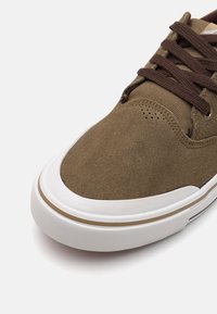 Brune semskede sneakers med en hvid gummisål, kontrasterende brune snørebånd og perforerede detaljer på tæerne for åndbarhed.