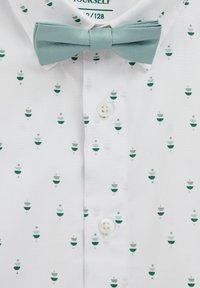 Camicia bianca con motivo verde di forme impilate. Presenta una cravatta a farfalla azzurro chiaro e un davanti con bottoni bianchi.