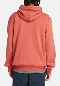 Sweat à capuche de couleur corail, à coupe décontractée, avec une texture douce et une poche kangourou. Accentué par un ourlet teal en dessous.