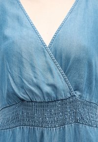 Kék farmer wrap ruha V-nyakú kivágással és széles, ráncolt derékrésszel.