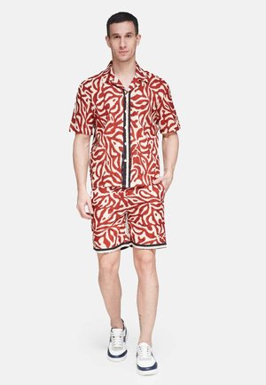 Short-sleeve red and white patterned shirt with matching shorts, featuring a black trim and geometric design details, worn with blue and white sneakers.
