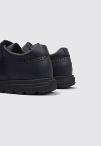 Zapatos de cuero azul marino con acabado suave, detalles perforados y suelas de goma negra texturizada. Forma redondeada con un diseño de perfil bajo.