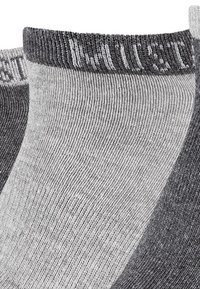 Calzini alla caviglia grigi e grigio scuro con un bordo a costine e testo. Il tessuto è morbido, con una texture liscia e un design aderente.