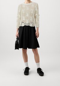 Kremowy sweter z dzianiny z otwartym koronkowym wzorem, czarna rozkloszowana spódnica, czarne trampki i białe skarpetki, trzymane w małej czarnej torebce.