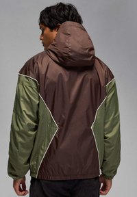 Ruskea ja vihreä huppari, kevyt materiaali, kontrastipaneelit ja valkoiset saumaraidat. Kuminauhakäärmeet hihoissa ja vyötäröllä.