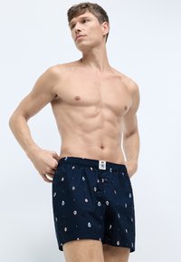 Marineblå boxershorts lavet af bomuld med en let tekstur, der har et gentaget mønster af cirkulære grafikker og en elastisk talje.