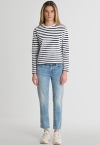 Baltas un tumši zils svītrains krekls ar garām piedurknēm, apvienots ar gaiši ziliem džinsiem. Ikdienīga piegriezne ar vienkāršu apaļu kakla izgriezumu. Ausi uz augšu papildina šos apģērbos.