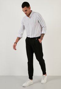 Camicia di lino a righe bianche, pantaloni neri affusolati e sneakers bianche. La camicia ha colletto button-down, maniche arrotolate e una texture sottile.