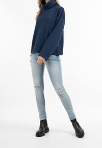 Pullover blu navy con colletto alto e maniche lunghe, abbinato a jeans chiari strappati e stivaletti neri con suola spessa.