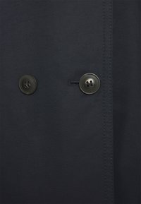 Dos botones oscuros cosidos en una tela oscura con costuras visibles y un ojal entre ellos.