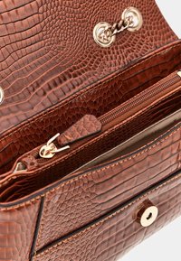 Interno di una borsa a mano in pelle marrone con rilievi, caratterizzato da una tasca con cerniera, dettagli in hardware dorato e un motivo testurizzato simile a quello di un rettile.