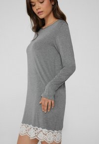 Vestido gris de mangas largas con escote redondeado y detalle de encaje blanco en el dobladillo. Textura suave con un corte relajado, que llega a mitad de muslo.