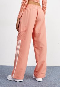 Vaaleanpunaiset cargo-housut, joissa on joustava vyötärö, sivutaskut ja valkoiset raidat lahkeissa. Valmistettu sileästä, kevyestä kankaasta.