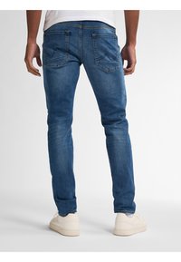 Blå denimjeans med smal passform, med två bakfickor med en subtil sömnad detalj, och kombinerade med vita sneakers.