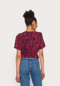 Rotes Oberteil mit floralem Muster, kurzen Ärmeln, leicht verkürztem Design und gerafftem Stoff an der Taille, kombiniert mit hochtaillierten Jeans.