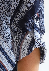 Chemise à manches longues dans des tons bleus avec des motifs floraux et cachemire. Détail de boutons aux poignets et texture variée du tissu.