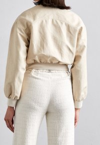 Beige bomberjack met opgeblazen mouwen, een aangesnoerde zoom, gecombineerd met textuur white hoge taille broeken met een gevlochten riemdetail.