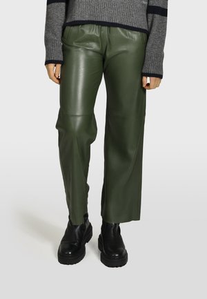 Pantalons en cuir vert à coupe décontractée et jambes droites, avec des coutures visibles et une taille haute. Associés à des bottines noires à talons épais.