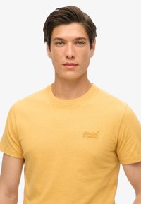 Gul bomulds T-shirt med rund hals og korte ærmer. Har et broderet logo på brystet. Glat tekstur, afslappet pasform.