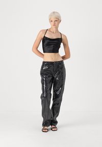 Un crop top en satin noir avec des fines bretelles associé à un pantalon noir pailleté. Les pantalons ont une coupe ajustée et un léger éclat, complétés par des sandales noires.