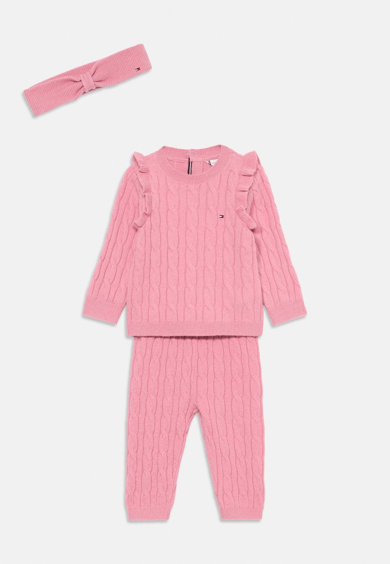 Rosa gestricktes Set aus Pullover und Hose mit Zopfmuster, Rüschendetails an den Ärmel des Pullovers und passendem Kopfband. Weiche Textur.