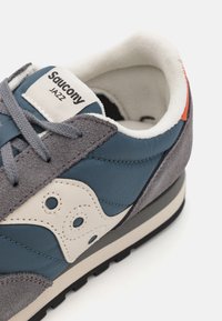 Saucony Jazz sneakers med en blanding av grå semsket skinn og blått stoff, med en hvit logo aksent og en teksturert gummisåle.