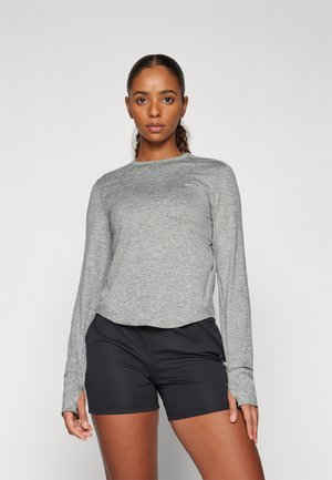 Camiseta atlética gris de manga larga con cuello redondo, diseño ajustado y orificios para los pulgares, combinada con pantalones cortos atléticos negros. Material texturizado y ligero.