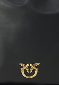 Black leather handbag featuring a textured surface and a gold-tone circular hardware accent with two stylized birds facing each other.
