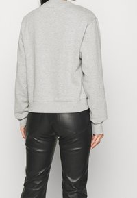 Šedá mikina s dlouhými rukávy, elastickými manžetami a volným střihem, kombinovaná s černými koženými kalhotami s hladkým povrchem a kapsami.