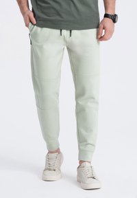 Lichtgroene sweatpants met elastische tailleband, voorzakken met rits en paneelstiksels; gecombineerd met beige veterschoenen.