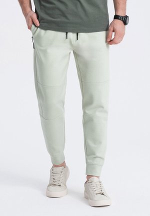 Light green sweatpants with elastic waistband, front zip pockets, and panel stitching; paired with beige lace-up shoes.