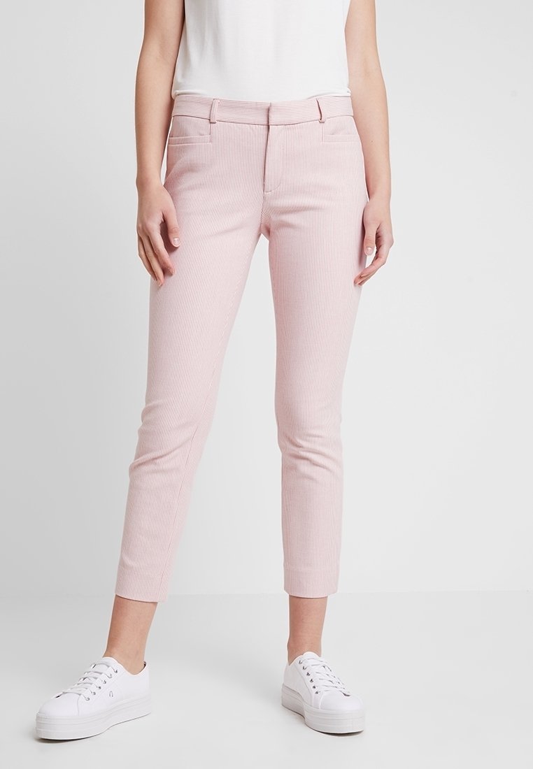 Light pink tailored trousers with subtle vertical stripes, slim fit, mid-rise waist, and front pockets, paired with white sneakers.