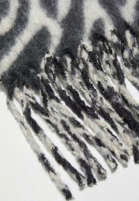 Écharpe en laine avec un motif abstrait gris et noir, ornée de franges sur les bords. Surface douce et texturée.