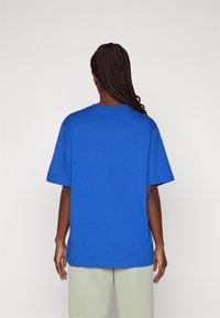 Kortärmad t-shirt med rund hals i enfärgad klarblå bomull. Lös passform med sänkta axlar, kombinerad med ljusgröna byxor.