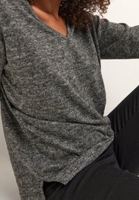 Haut à manches longues en maille texturée grise avec un col en V et des boutons décoratifs à l'ourlet. Associé à un pantalon noir slim.