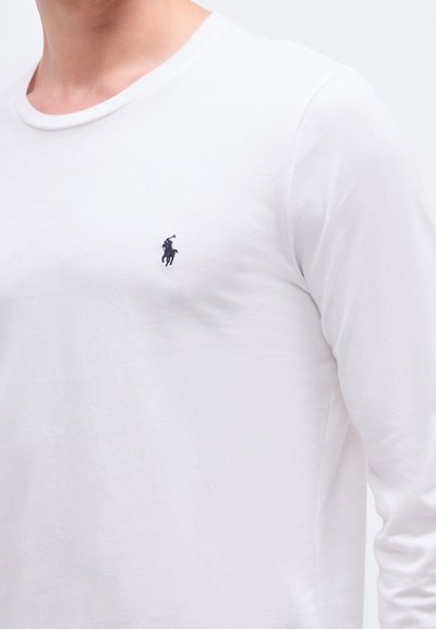 Langermet hvit bomulls-T-skjorte med rund hals og liten mørkeblå brodert logo på venstre bryst. Jevn tekstur.