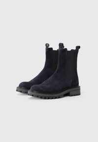Botines de ante azul marino con paneles laterales elásticos, lengüetas de tiro y suelas de goma negra resistentes. Presentan una textura suave y punta redonda.