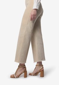 Beige vidde benbukser med frynsede kanter, parret med brune blokhæle sandaler med tynde stropper og ankelspænde.
