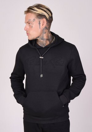 Hoodie noir en tissu doux avec une poche frontale, un cordon de serrage au cou, et un logo en relief "Pigeon x Paris" sur la poitrine.