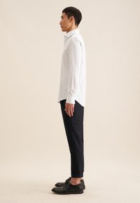 Camicia a maniche lunghe a quadri bianchi, pantaloni blu e scarpe nere. La camicia presenta un colletto a punta e una linea dritta.