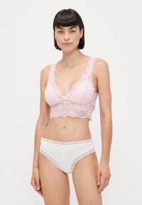 Rosa spissvokst bralette med brede stropper og bølgede kanter, sammen med hvite truser med blonder. Delikat, blomstrete blonderdesign gjennom hele.