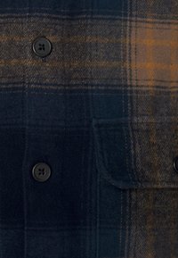 Geruite flanellen overhemd in donker marineblauw en bruine tinten, met een sluiting van vier knopen, een borstzak en een zachte textuur.