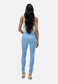Jeans skinny de color azul claro con cintura alta, que cuentan con un diseño de cinco bolsillos y un ligero desvanecimiento, combinados con sandalias de tacón alto blancas.