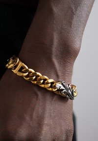 Goldene Metallkette mit einem Verschluss im Blattdesign mit Silberakzenten. Glatte Textur mit einem klobigen, ineinandergreifenden Linkstil.