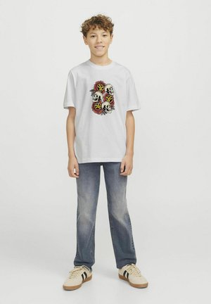 Witte katoenen t-shirt met een grafische afbeelding van schedels en bloemen in rood en zwart. Gecombineerd met lichtblauwe jeans en beige sneakers.